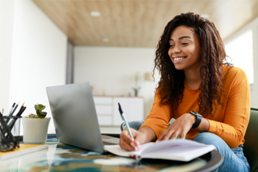 GettyImages-1370433251 Woman Sitting At Desk Working On Laptop And Taking Notes GettyImages-1370433251 Woman Sitting At Desk Working On Laptop And Taking Notes