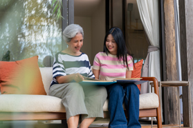 Elderly woman and granddaughter looking at photo album outdoors (high res)