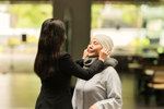 APAC - elderly woman gets help from her daughter with her cap (high res)