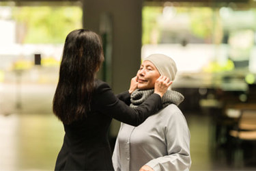 APAC - elderly woman gets help from her daughter with her cap (high res)