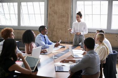 Female manager stands addressing team at board meeting-iStock-904596172