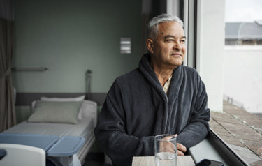 Senior patient gazing out window in hospital room (high res)