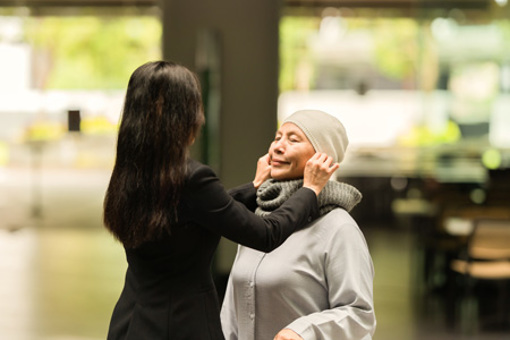 APAC - elderly woman gets help from her daughter with her cap (high res)