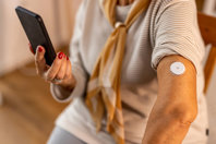 Woman checking blood glucose with smartphone-GettyImages-2191304337