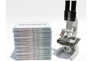 Stack of paper money with microscope-GettyImages-1631239006